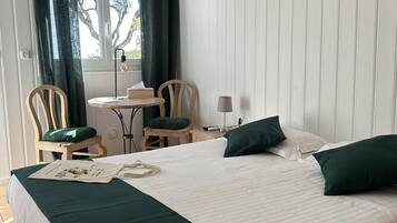 A hotel room with a large bed, two chairs, a small table, and a window with curtains.