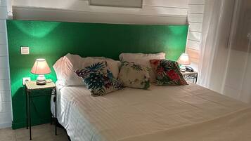 A bedroom with a green headboard, a bed with white bedding and floral pillows, two bedside lamps, and a framed picture on the wall.