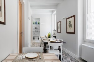 Un comedor con una mesa larga dispuesta para cuatro, sillas blancas y un tapete estampado.