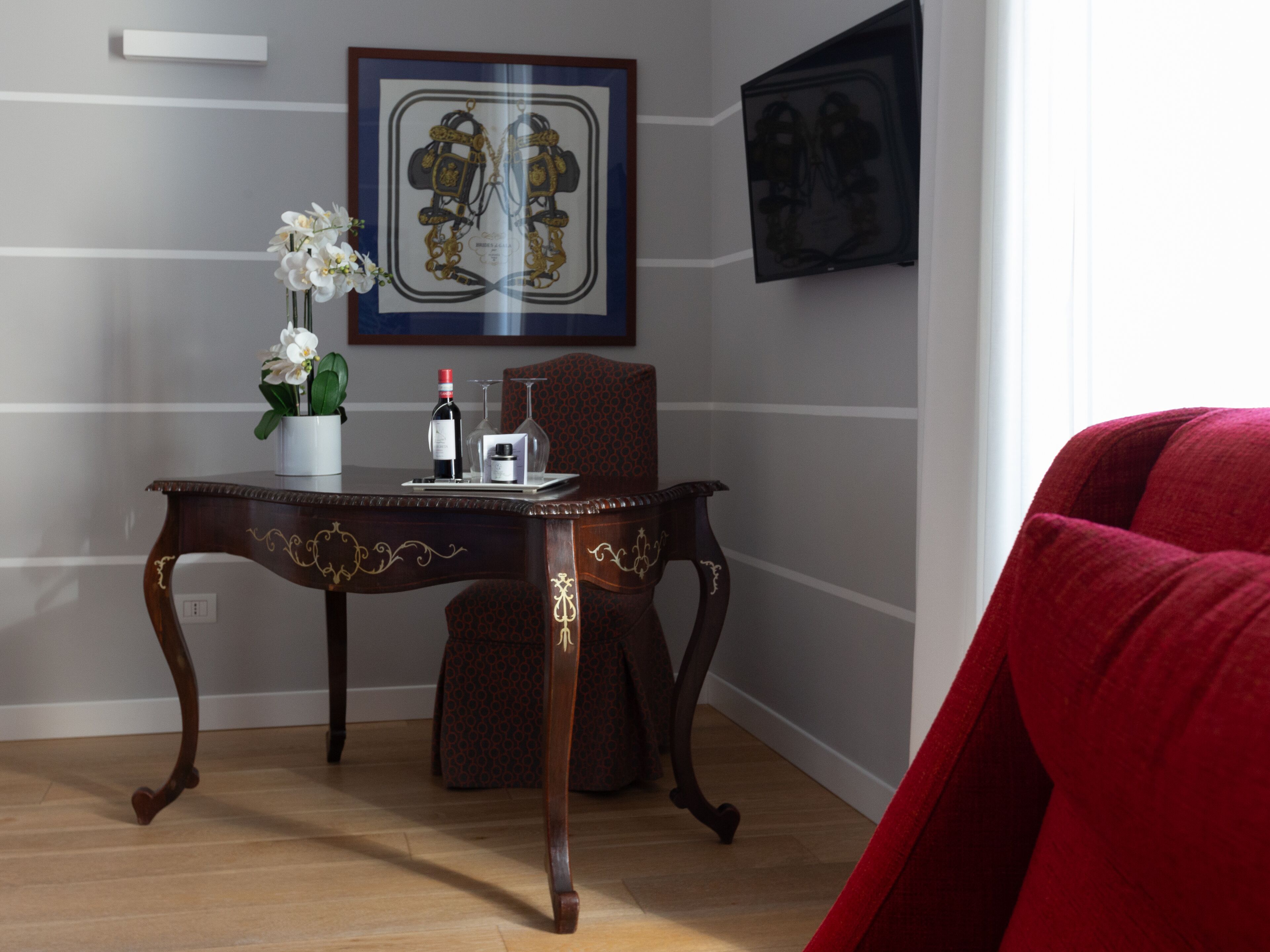Een kamer met een houten tafel, een stoel, een vaas met bloemen, een ingelijst schilderij en een rode stoel.
