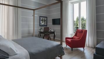 Una habitación de hotel moderna con cama con dosel, un sillón rojo, una mesita con una planta y un televisor montado en la pared.
