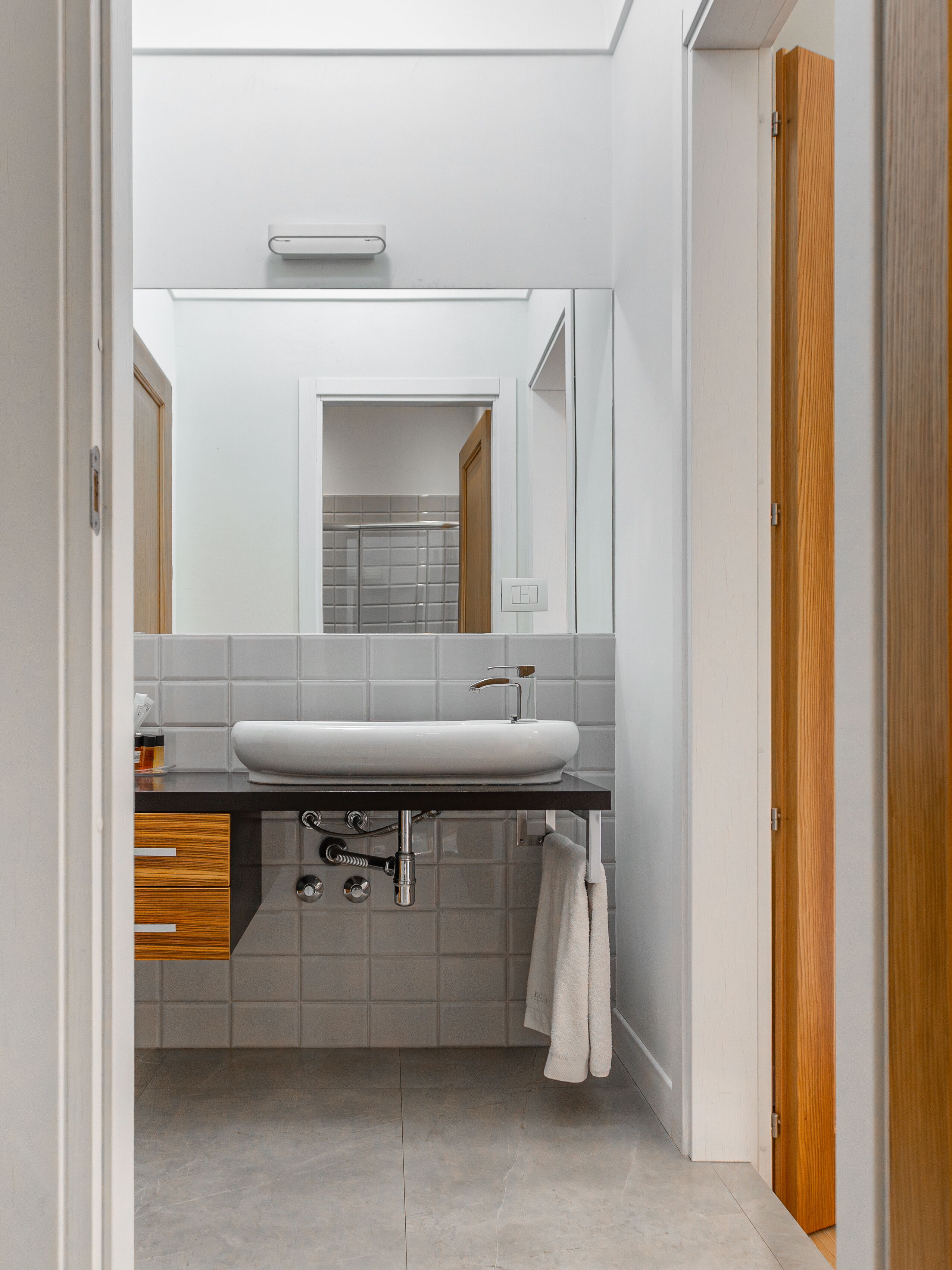 A modern bathroom with a white sink, a mirror, and a towel hanging on the wall.