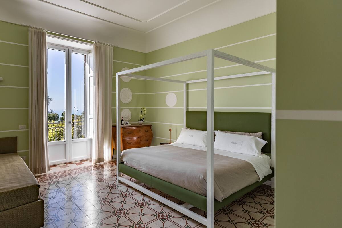 A bedroom with a four-poster bed, a wooden dresser, and a view of the outdoors through a sliding glass door.