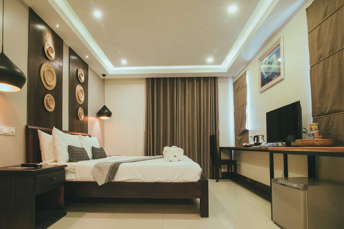 Una habitación de hotel con cama, mesita de noche, lámpara, cortinas y un escritorio con silla.