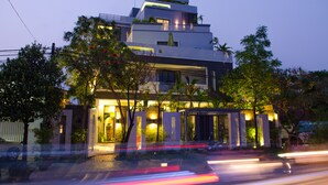 A modern multi-story building with a well-lit entrance and landscaped surroundings. - Hotel Five.S (Kampot)