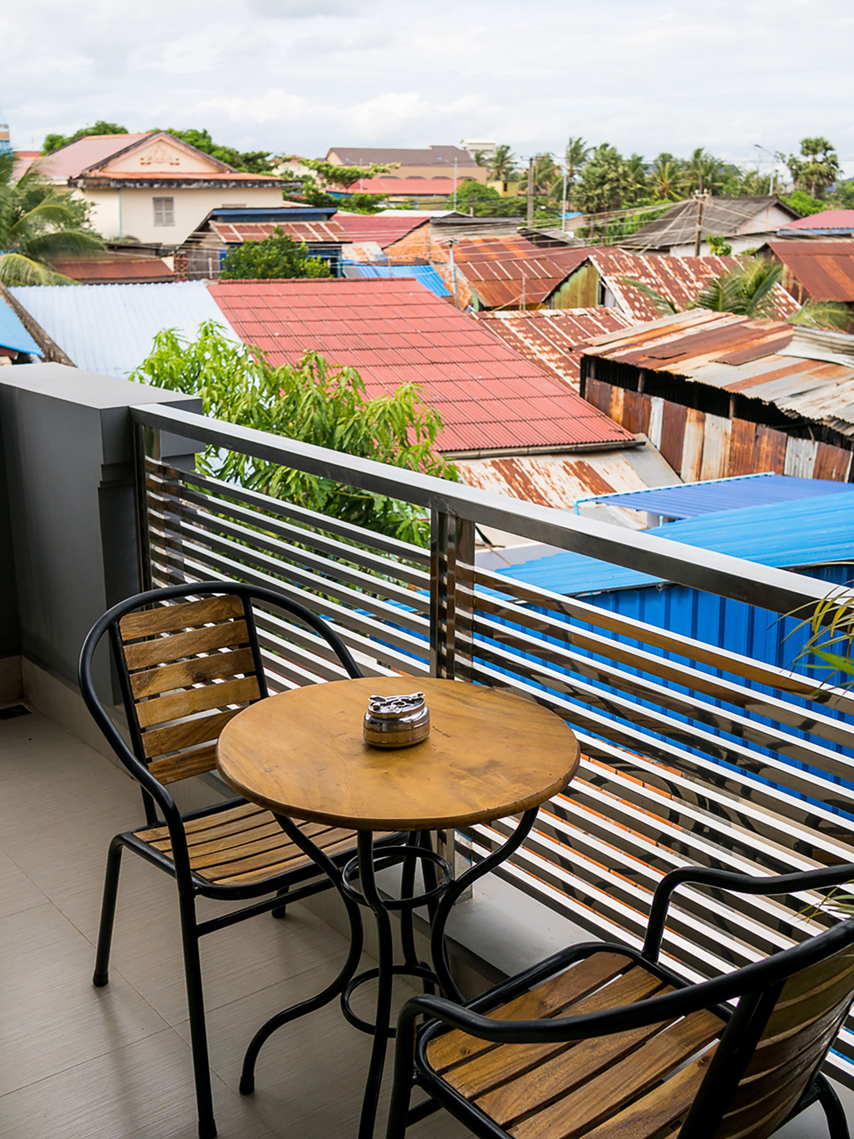 A balcony with a table and two chairs, overlooking a residential area with colorful buildings.