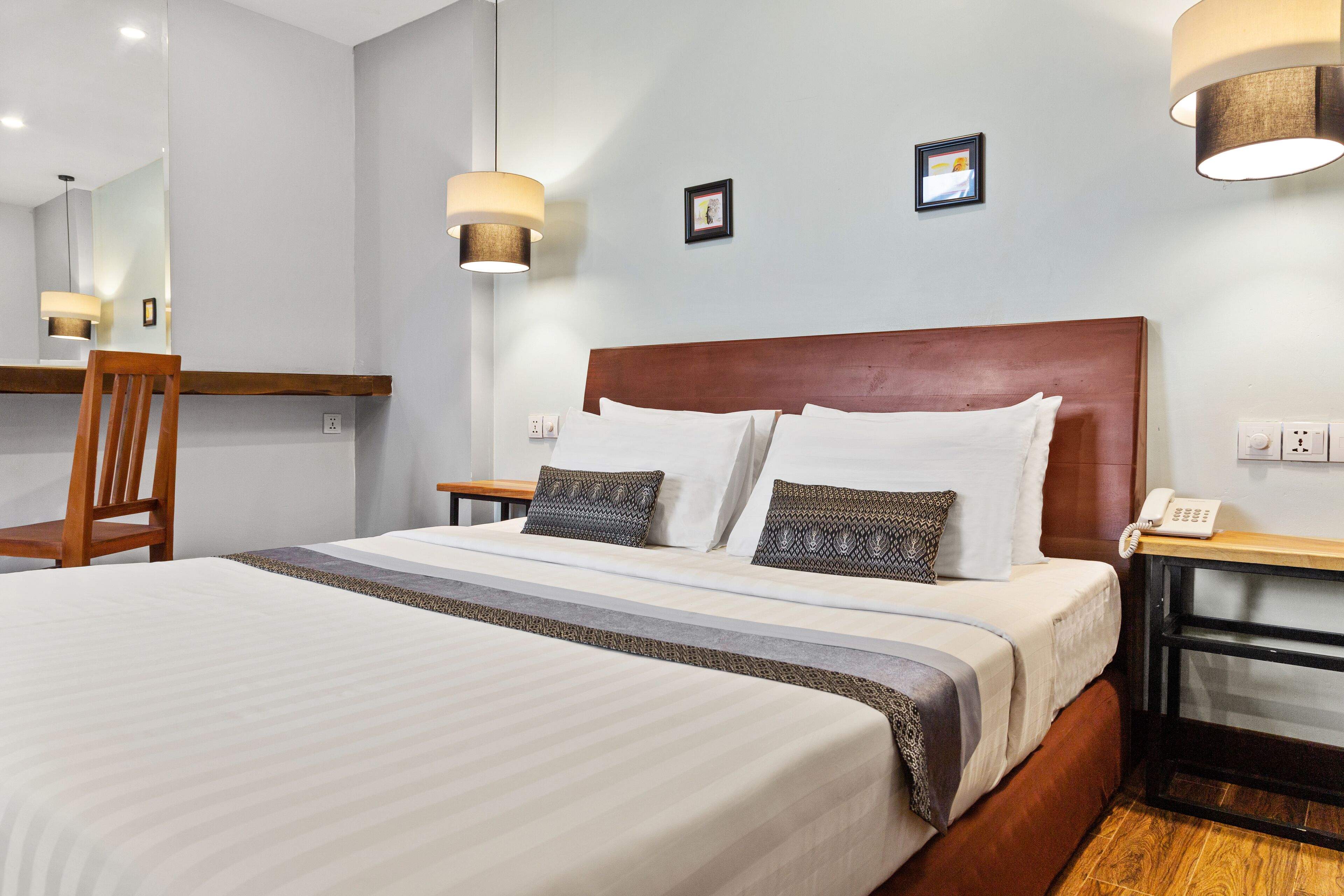 A neatly made bed with a wooden headboard, a bedside table with a lamp, and a mirror on the wall.