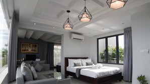 A modern hotel room with a large bed, a sofa, a glass coffee table, and a dining area. There are pendant lights and a large window with curtains. - Hotel Five.S (Kampot)