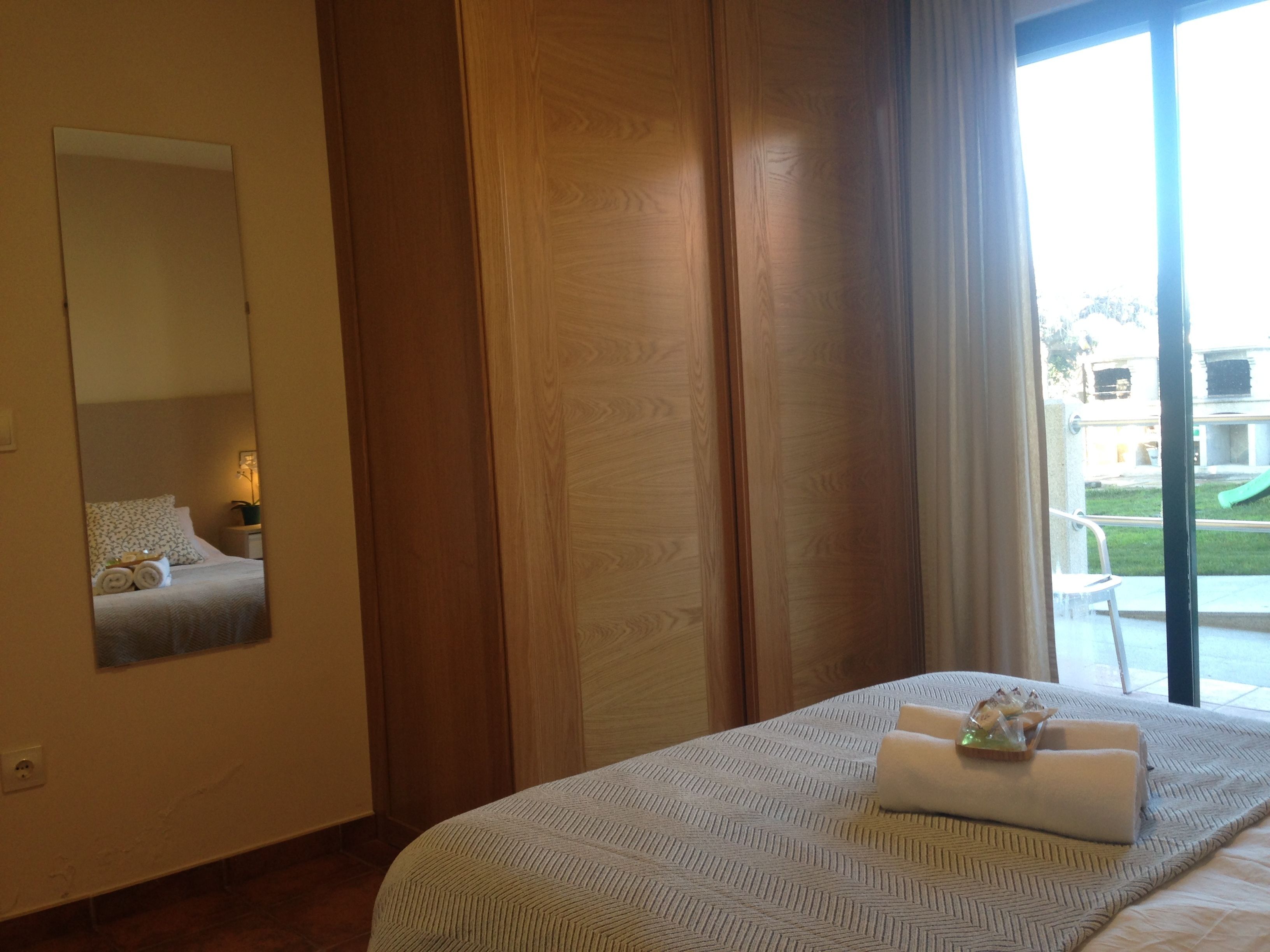 A hotel room with a bed, a large mirror, a window with curtains, and a view of the outside.