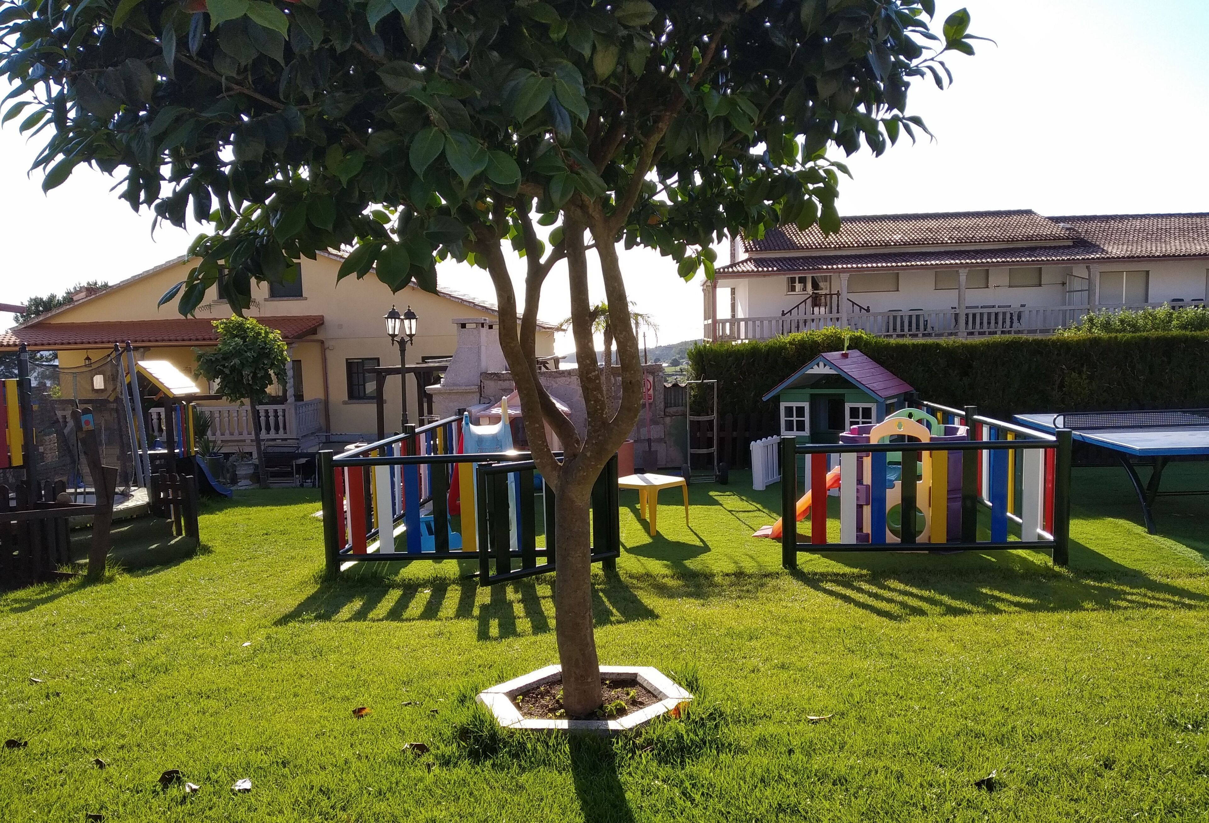 A playground with colorful play structures, a tree, and a building in the background.