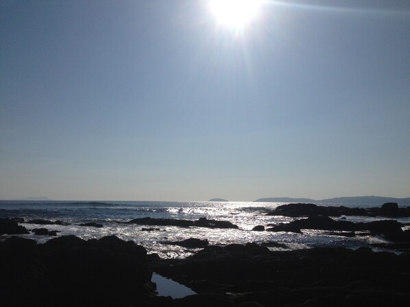 A coastal scene with sunlight reflecting off the water and rocks. - Apartamentos Aqualecer (Sanxenxo)