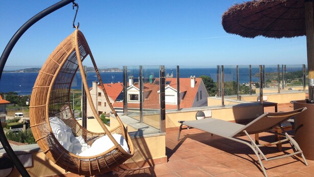 Ein Balkon mit Korbschaukel, Liegestuhl und Strohdachschirm.