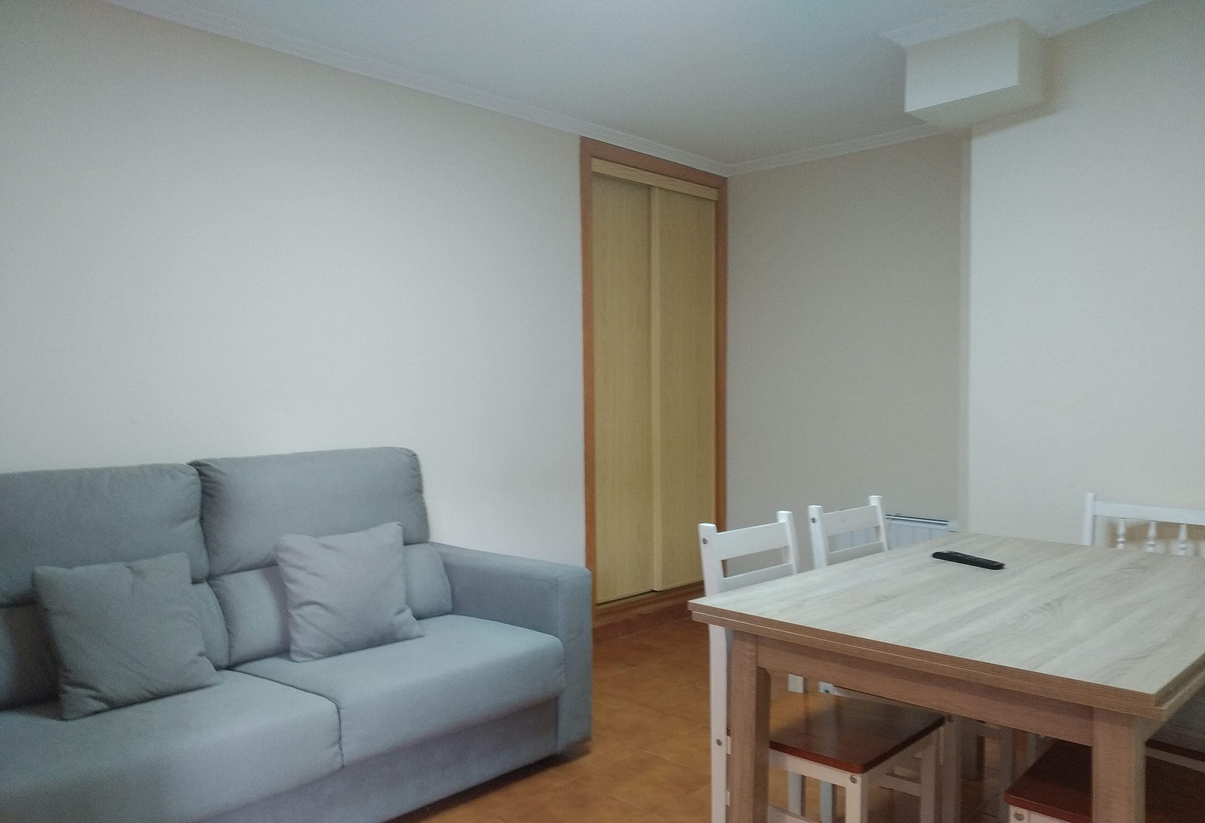 A room with a light blue sofa, a wooden dining table with four chairs, and a closed door.