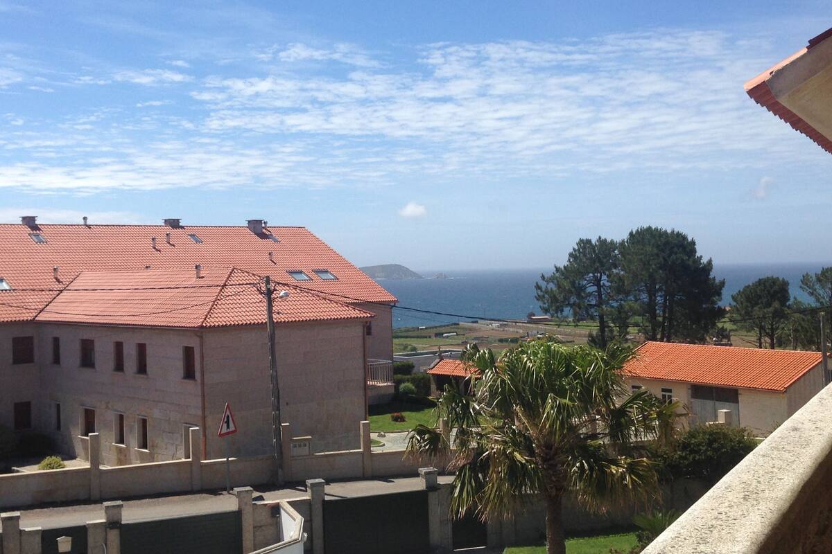 A coastal residential area with red-tiled roofs, a palm tree, and a view of the sea.