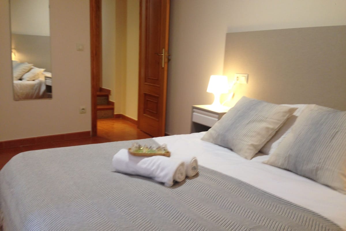 A neatly made bed with a white comforter and pillows, a tray of towels, and a lamp on a bedside table.