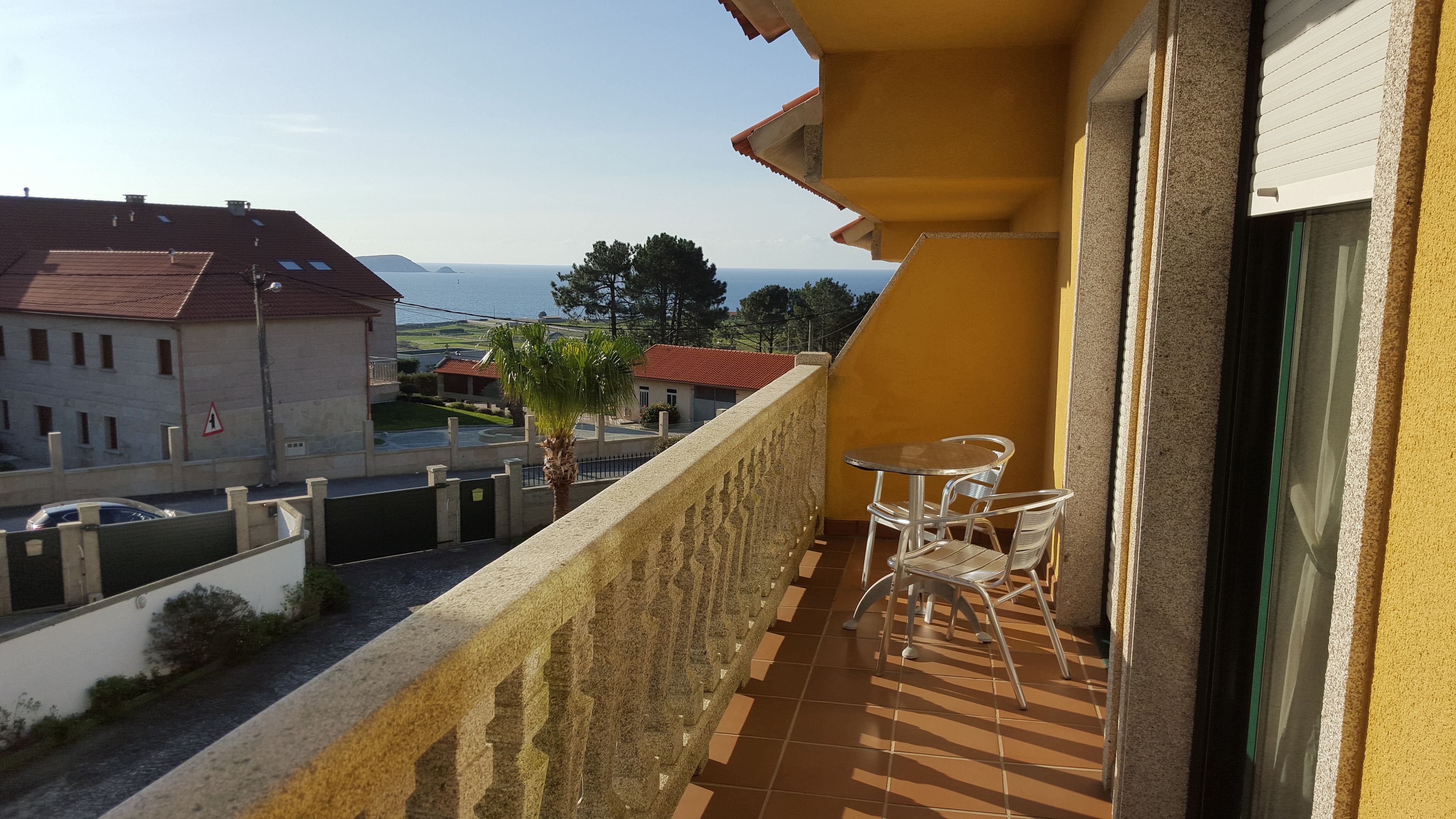 A balcony with a view of the sea, a small table, and chairs.