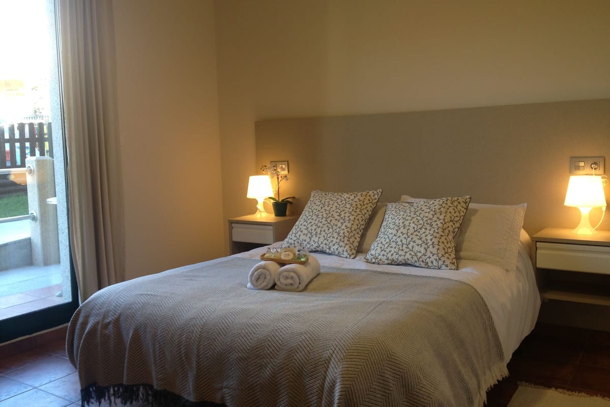 A neatly made bed with a patterned bedspread, two bedside lamps, and a small potted plant on the nightstand.