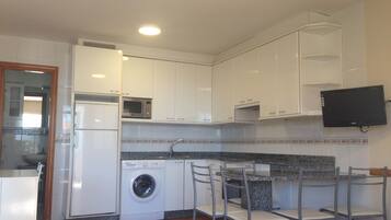 A compact kitchen with white cabinets, a washing machine, a microwave, and a TV mounted on the wall.