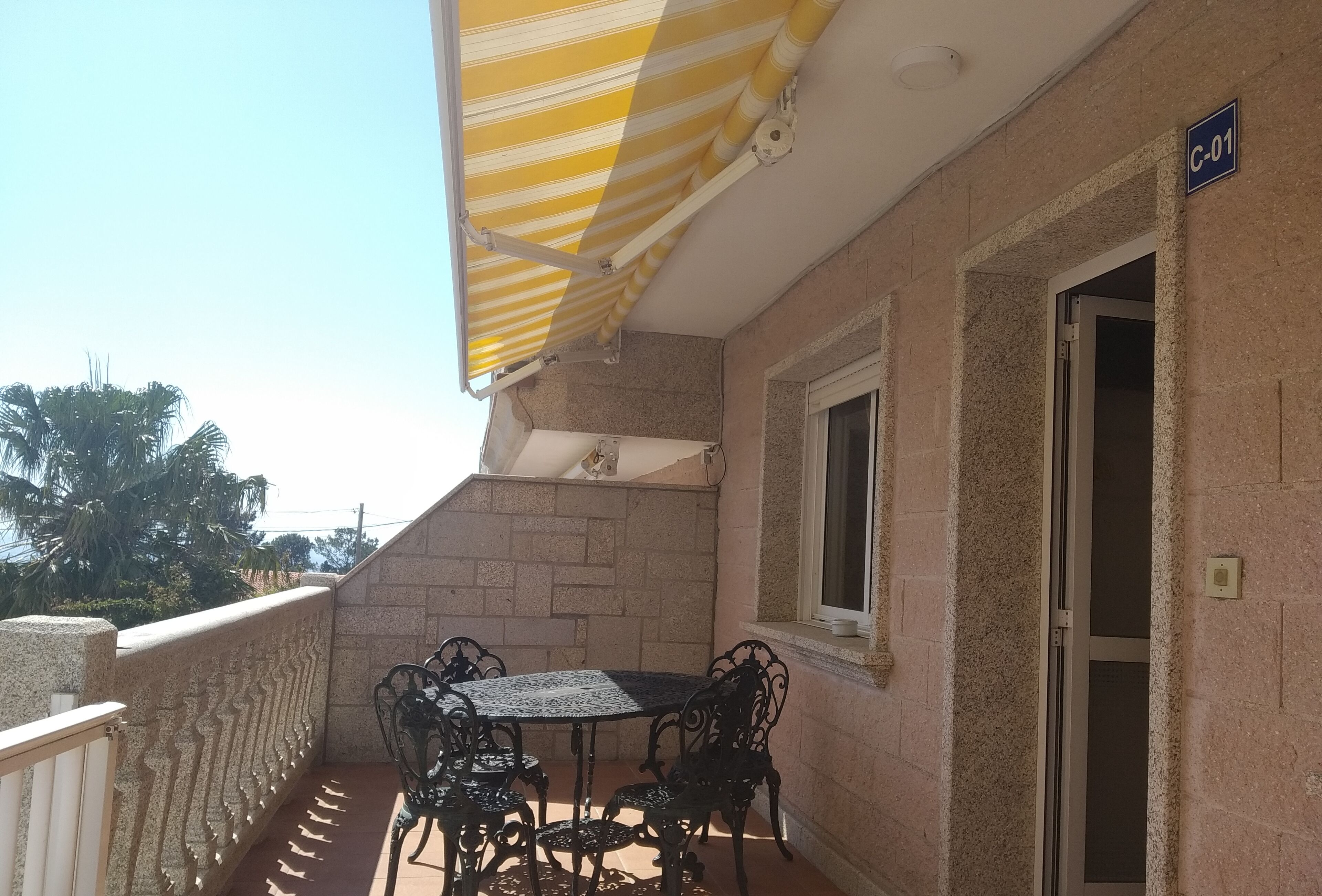 A balcony with a table and chairs, a striped awning, and a door marked "C-01".