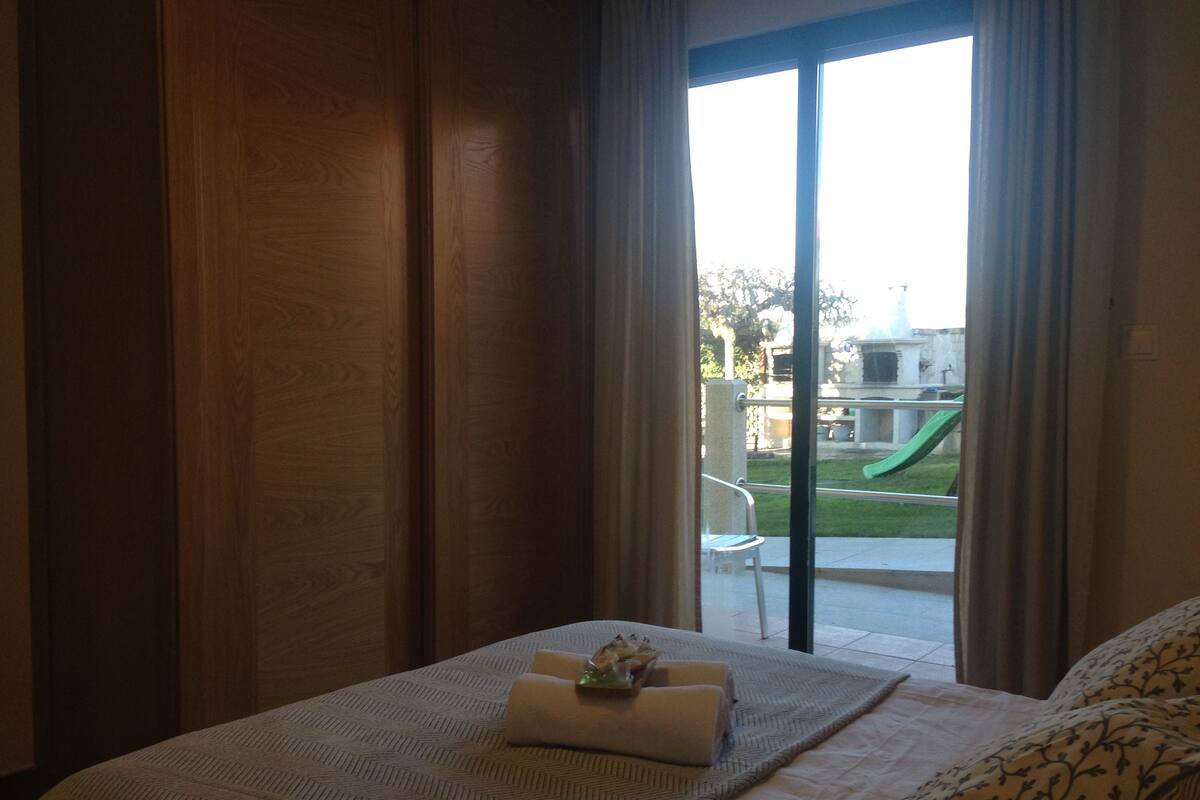 A hotel room with a bed, a view of a playground through a glass door, and a window with curtains.
