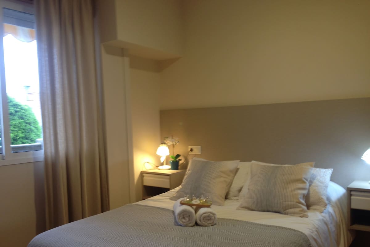 A hotel room with a bed, a nightstand with a lamp, and a window with curtains.