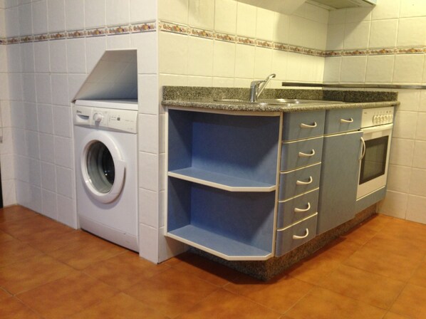 A compact kitchen with a built-in washing machine, a sink, and a stove. - Apartamentos Aqualecer (Sanxenxo)