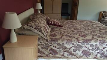 A bedroom with a bed, two bedside lamps, a wooden nightstand, and a wardrobe.