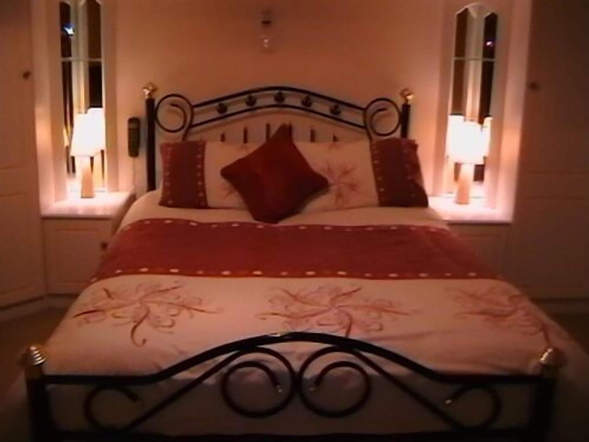 Een net opgemaakt bed met een metalen frame, twee kussens en een rode deken.
