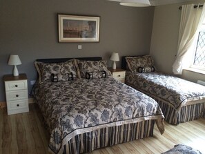 Quarto com duas camas, mesa de cabeceira com abajur, aparador com gavetas, quadro pendurado na parede e janela com cortinas.