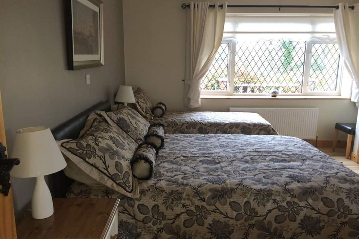 Een slaapkamer met twee bedden, een raam met gordijnen, een nachtkastje met een lamp en een lijst met een afbeelding aan de muur.