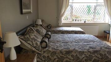 A bedroom with two beds, a window with curtains, a bedside table with a lamp, and a framed picture on the wall.