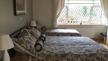 A bedroom with two beds, a bedside table with a lamp, a window with curtains, and a radiator.