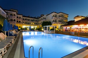 Ein Schwimmbecken mit Liegestühlen und Sonnenschirmen, umgeben von Gebäuden mit Balkonen und einer Bar.