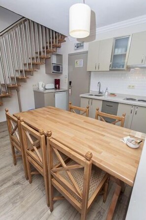 Cozinha moderna com mesa e cadeiras de madeira, uma escada e um micro-ondas.