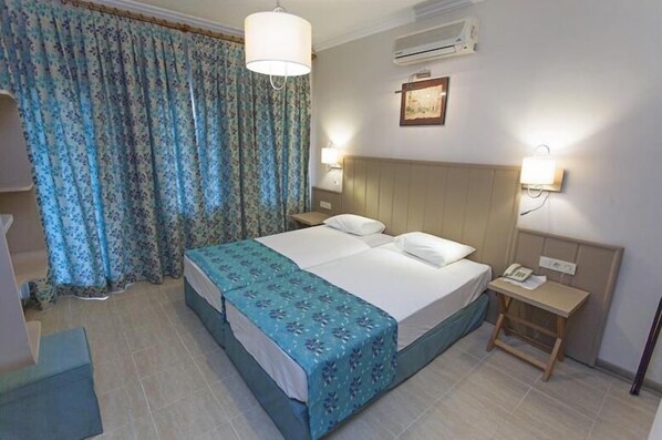 Une chambre d’hôtel avec un lit, des rideaux, une table de chevet avec un téléphone et un appareil de climatisation fixé au mur.