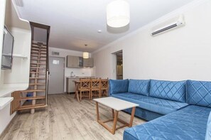 Uma sala de estar moderna com um sofá azul, mesa de madeira e uma escada que dá para uma cozinha.