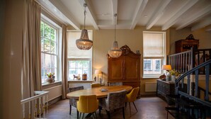 A dining area with a wooden table and yellow chairs, a chandelier, and a staircase with a railing. - City House Grande Madame Agaath (Leeuwarden)