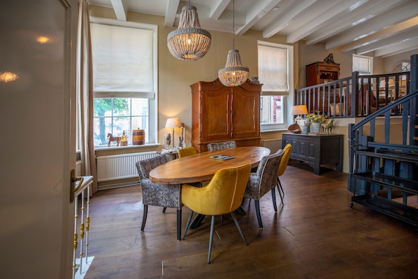 A dining area with a wooden table and chairs, a chandelier, and a view of the outside through large windows. - City House Grande Madame Agaath (Leeuwarden)