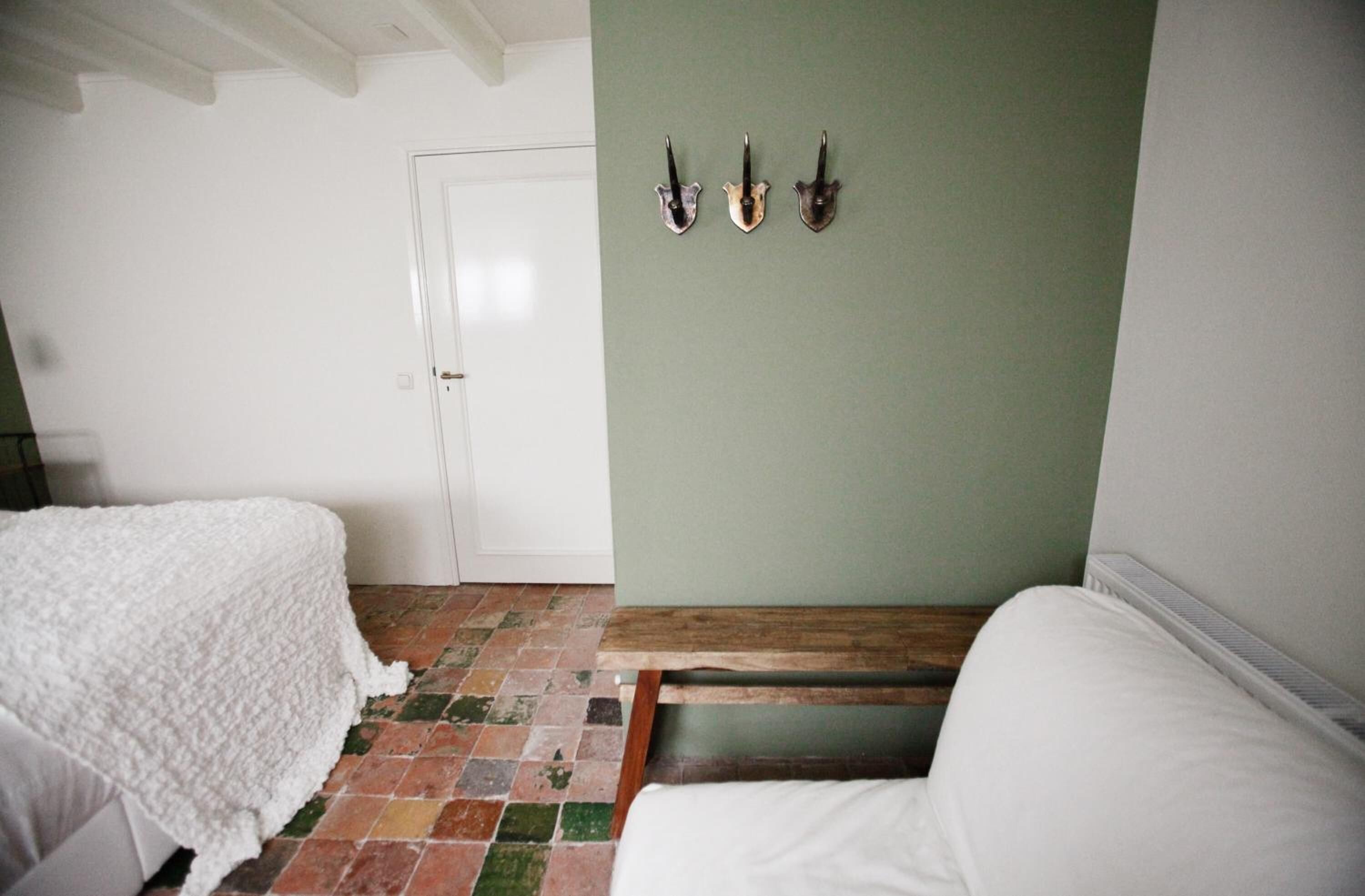 A room with two beds, a green wall, and a tiled floor.