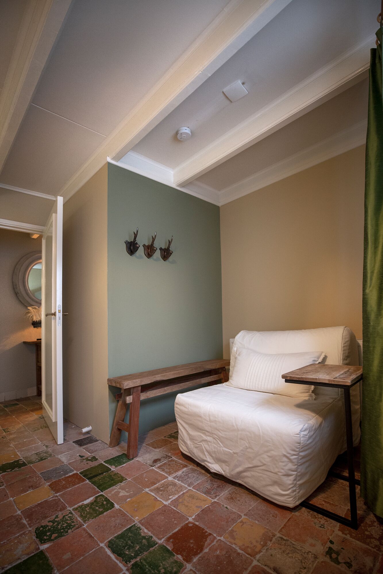 A small, cozy room with a single bed, a wooden bench, and a wall-mounted shelf.