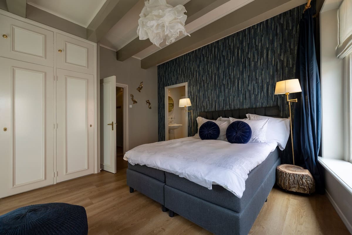 Une chambre à coucher avec un lit, une lampe de chevet, un plancher en bois et une fenêtre avec des rideaux.
