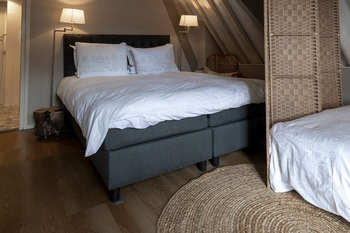 Une chambre à coucher avec un lit, deux lampes de chevet, une chaise en osier et un plancher en bois.