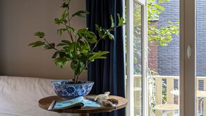 A bedroom with a bed, a bedside table with a blue and white bowl, a potted plant, and a view of the outside balcony. - City House Grande Madame Agaath (Leeuwarden)