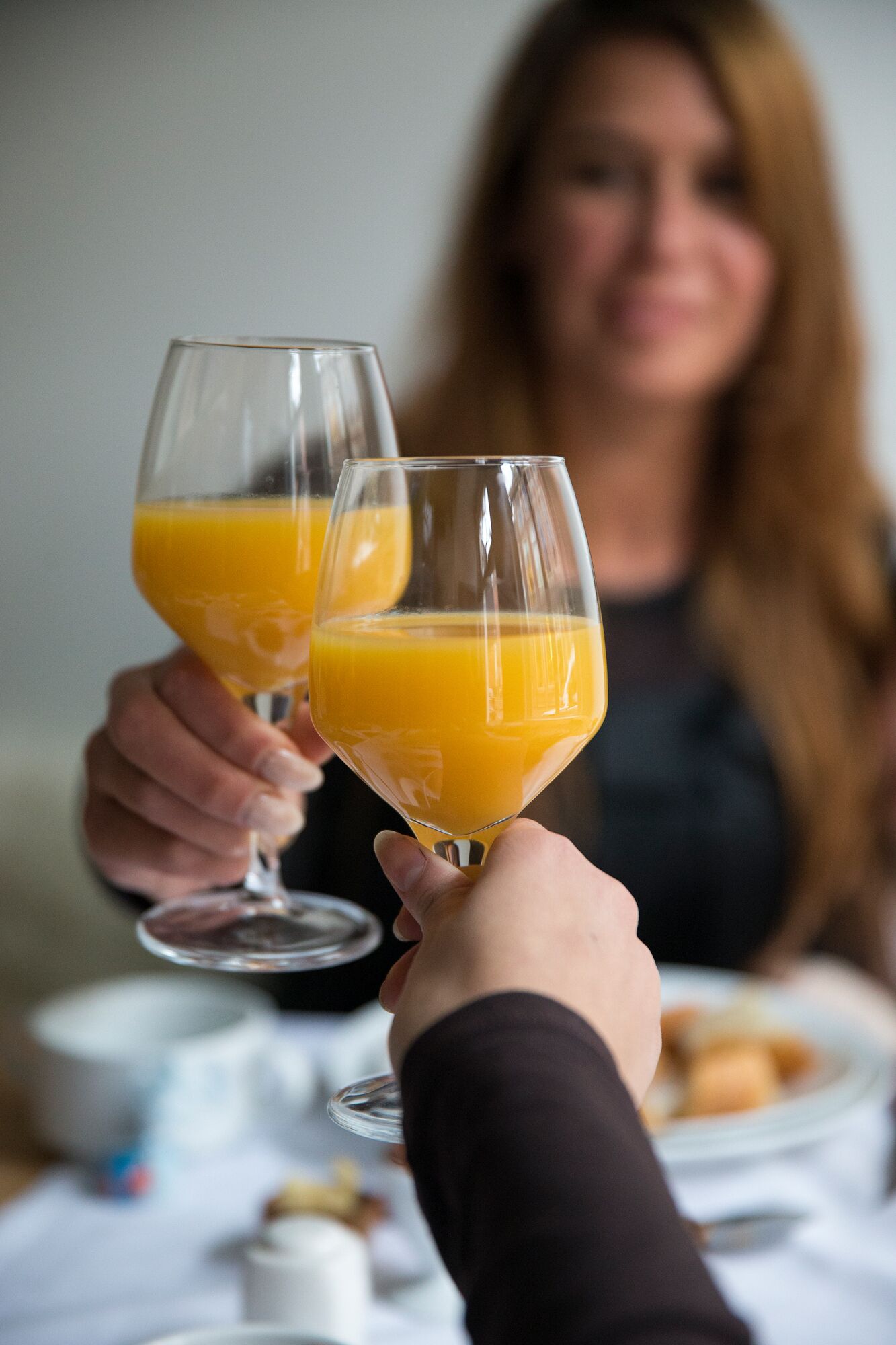 Kaksi ihmistä istuu pöydän ääressä, ja heillä on käsissään lasit, joissa on appelsiinimehua. Pöytä on peitetty valkoisella pöytäliinalla.