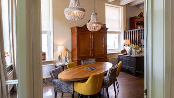 A dining area with a wooden table and chairs, a chandelier, and a view into another room with a window.