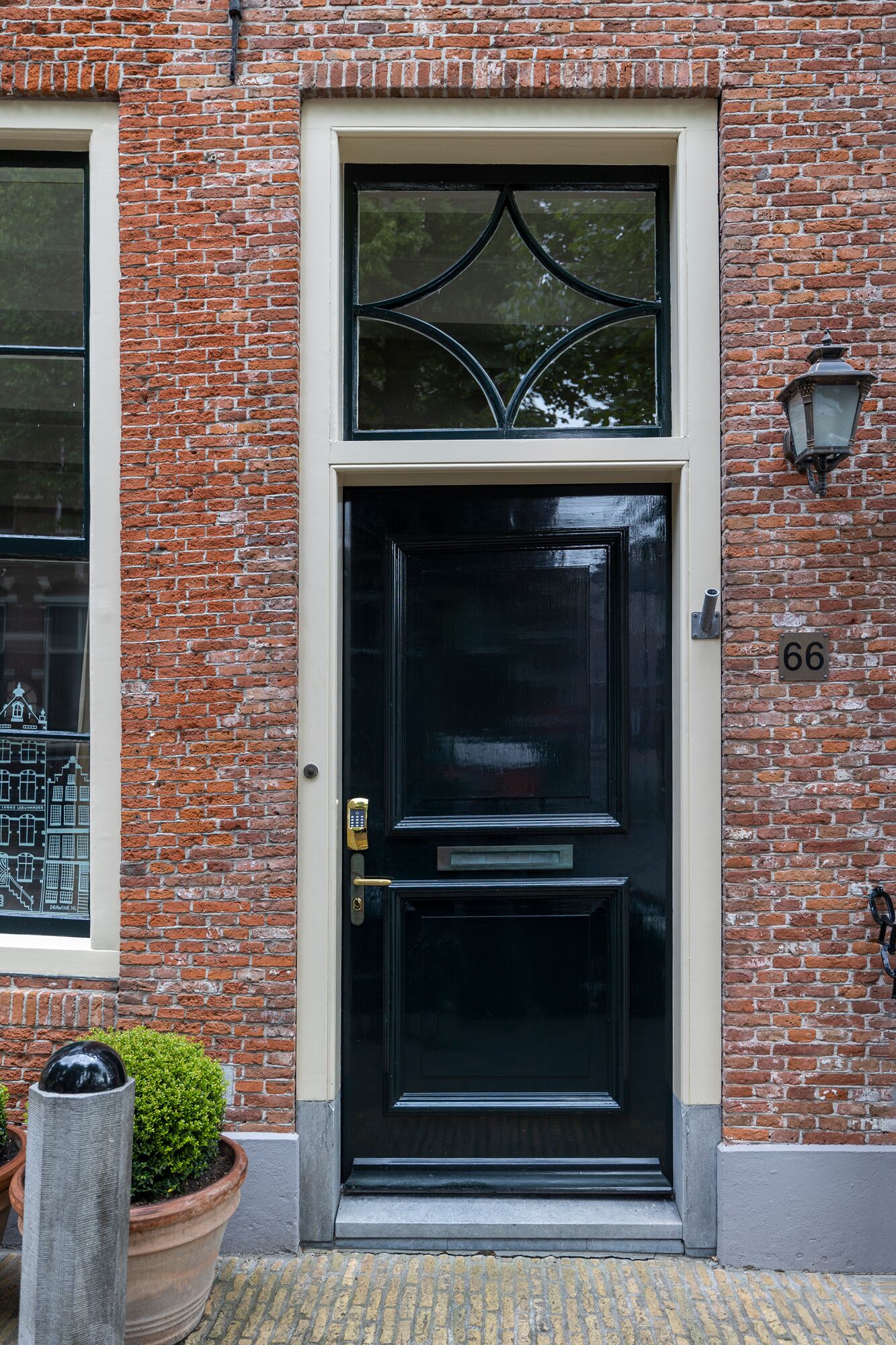 A black door with a brass handle and a keypad lock, set in a brick building with a window to the left.