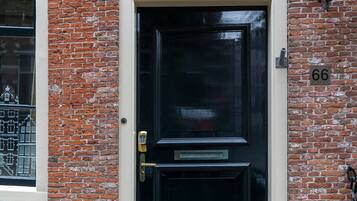 A black door with a brass handle and a keypad lock, set in a brick building with a window to the left.