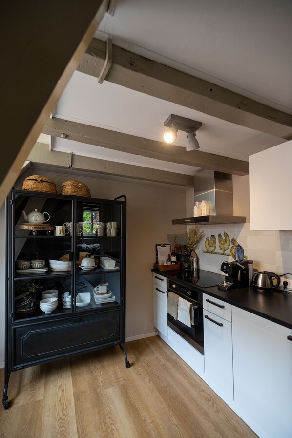 A kitchen with a black cabinet filled with dishes, a coffee machine, and a tiled backsplash with a chicken design. - City House Grande Madame Agaath (Leeuwarden)