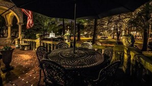 Un patio al aire libre con una mesa redonda y sillas, rodeado de muros de piedra y macetas con plantas.