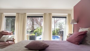 A bedroom with a bed, a nightstand, a lamp, and a view of an outdoor swimming pool. - B&B Filemon & Baucis (Bruges)